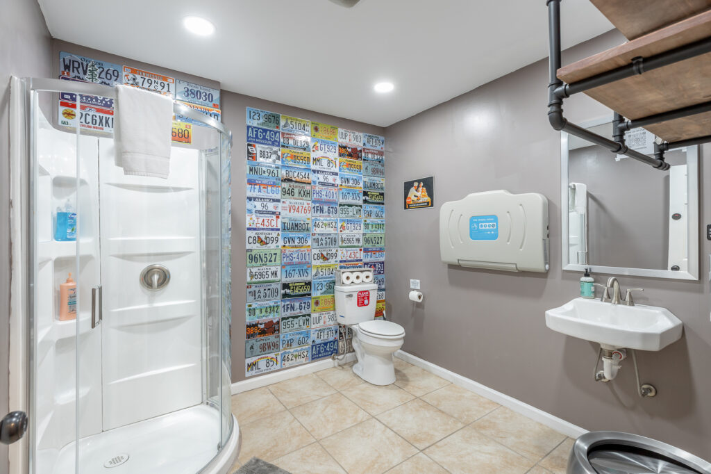 Rock Spring Resort event center bathroom with glass shower, toilet, baby changing station, and license plate feature wall.