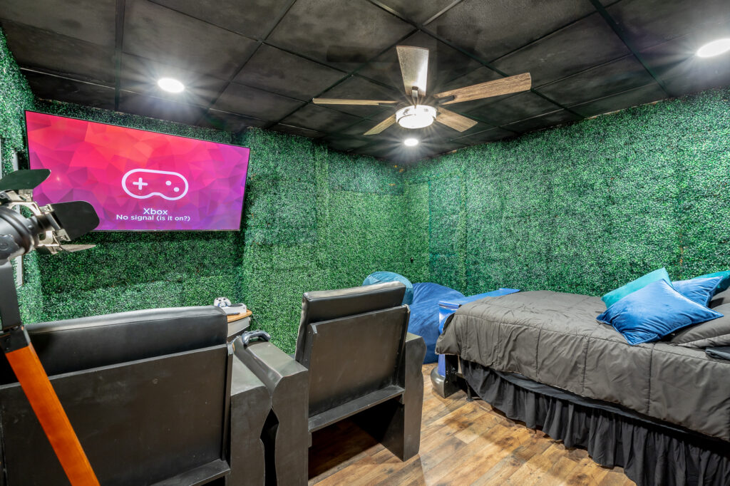 Entry view of the game room bedroom at Rock Spring Resort with smart TV, bed, custom chairs, and boxwood accent walls.