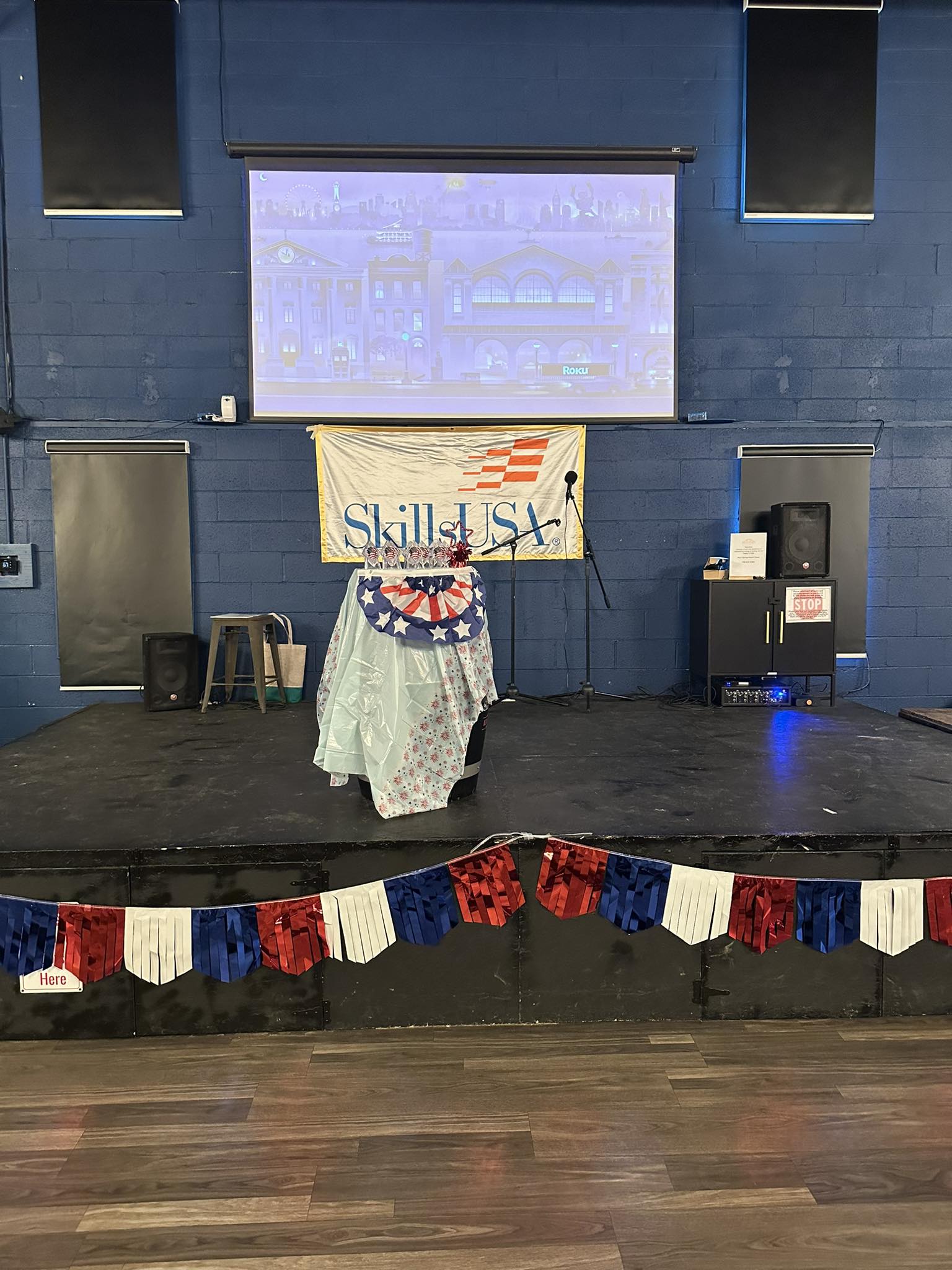 Rock Spring Resort event center stage set up for SkillsUSA ceremony with patriotic bunting, microphones, projector, and barrel podium