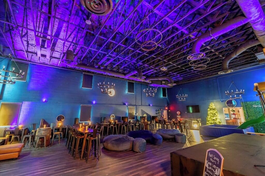 Wide-angle view of Rock Spring Resort's event center showing seating, bean bags, stage, bar, and custom lighting projected on vaulted ceiling.
